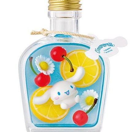 A clear glass bottle with a gold cap, containing a blue liquid and various colorful fruits and flowers, including cherries, daisies, and lemon slices.