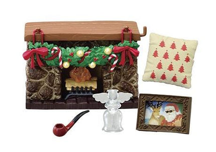 a miniature fireplace with a Christmas wreath, a red and white pillow, a pipe, a small glass object, and a picture frame.