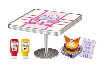a table with a pink and white design, a yellow mustard bottle, a red ketchup bottle, a small toy figure, and a small toy hamburger.