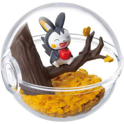 A figurine of a character from the Pokemon franchise is sitting on a branch inside a glass ball, surrounded by yellow leaves and a pile of yellow leaves.