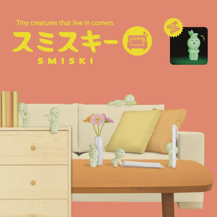 The image is a collage featuring a living room scene with various objects, including a couch, a coffee table, and several small figurines. The text in the image is in Japanese and reads "Tiny creatures that live in corners" and "SMISKI".