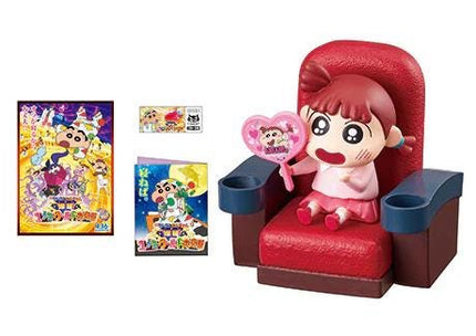 A toy figurine of a young girl sitting in a red chair, holding a heart-shaped object, and a poster or album featuring the same character.