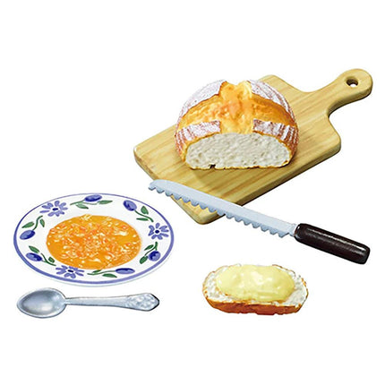 a wooden cutting board with a loaf of bread, a plate of soup, a spoon, and a knife.