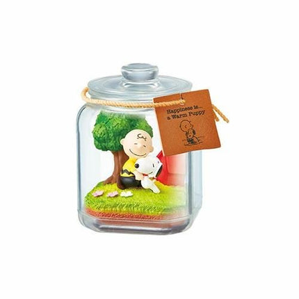 A figurine of a character from the Peanuts comic strip, including a dog, is displayed inside a glass jar with a label that reads "Happiness is a Warm Puppy".