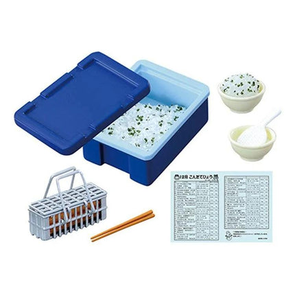 various food items and utensils, including a blue container with rice, a small plastic basket, chopsticks, and a blue and white instruction sheet.