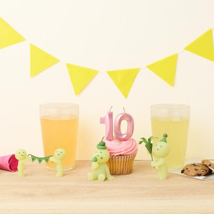 a birthday celebration with a cupcake, two glasses of drink, and a number 10 candle. There are also small figurines of people and a banner with yellow triangles hanging on the wall.