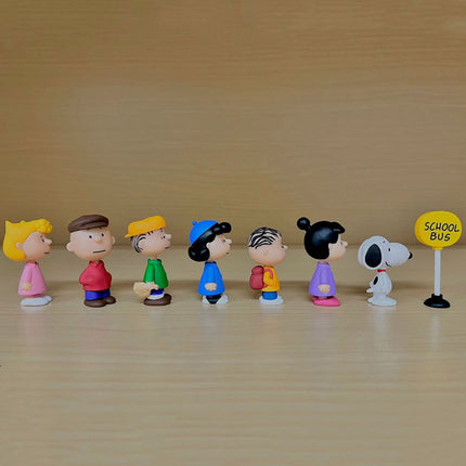 Seven Peanuts capsule toy figures standing side by side, with a school bus sign