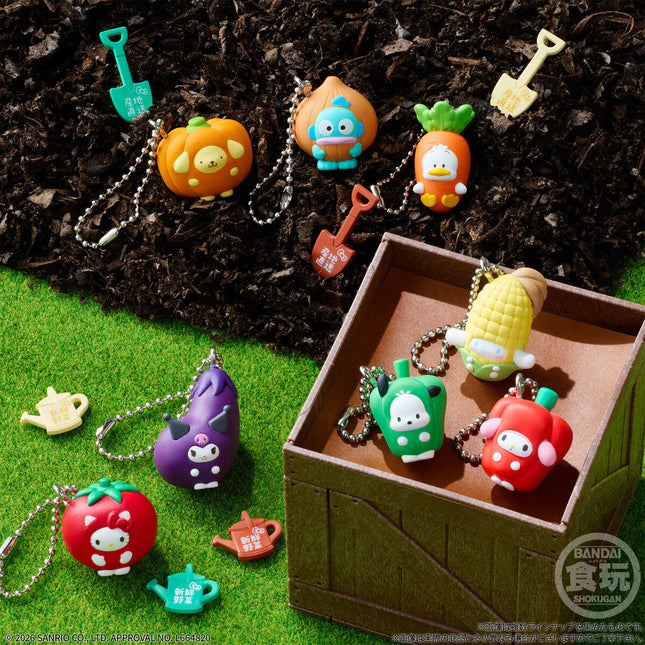 Vegetable character charm keychains scattered on grass around a wooden display box