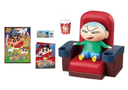 A toy figurine of a cartoon character sitting in a red chair, with a cup and a poster of the same character nearby.