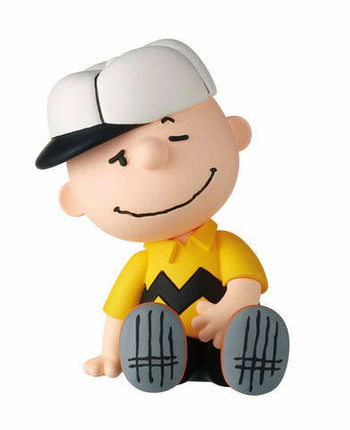 Charlie Brown-style capsule toy figure in yellow shirt and black cap, seated