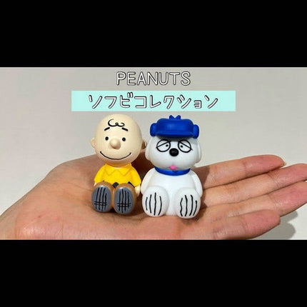 Hand-held pair of PEANUTS capsule toy figures: boy in yellow shirt and blue-hat dog.