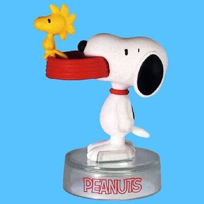 Peanuts Snoopy figure holding yellow star toy, wearing red outfit, on round "PEANUTS" base
