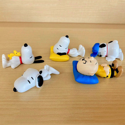 Snoopy and friends capsule mascot figures laid out on a wood surface