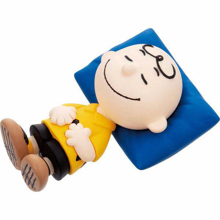 Charlie Brown capsule mascot figure lying on a blue pillow with yellow outfit