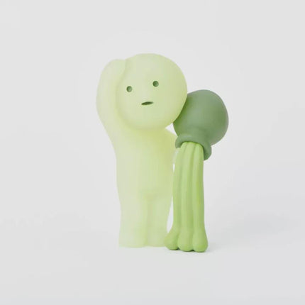 A small, glowing green figurine with a long, tube-like body and a round head, holding a green object in its hand.