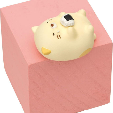 A small, yellow cat figurine is sitting on top of a pink block.
