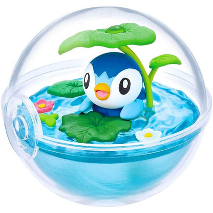 A small blue and white penguin figurine is sitting in a transparent glass ball filled with water, surrounded by green leaves and flowers.
