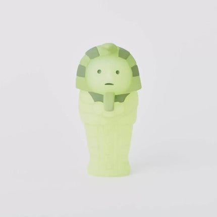 A small, green figurine of a mummy or mummy-like figure, with a distinctive headdress and a somewhat eerie appearance.