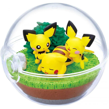 A transparent glass terrarium containing three yellow Pokemon figurines, including Pikachu, in a miniature garden setting.