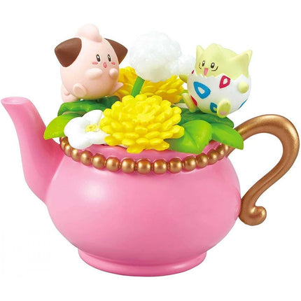 A pink teapot with a gold handle and a small figurine of a pink pig sitting on top of a flower arrangement.