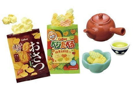 various snacks and a teapot, including a bag of chips, a teapot, and a bowl of chips.