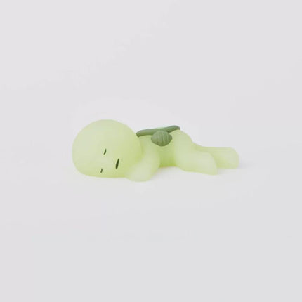 A small, glowing green figurine is lying down on a white background.