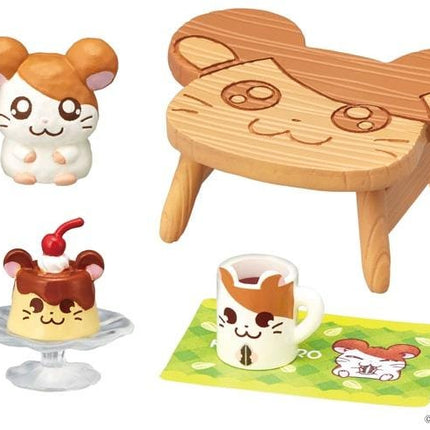 a variety of cute and whimsical items, including a hamster figurine, a wooden chair with a cat face design, a dessert with a cherry on top, a mug with a cat face design, and a small toy hamster.