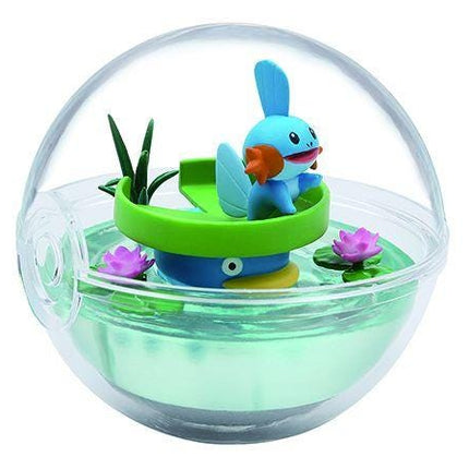 A figurine of a blue fish with orange fins is sitting on a green boat in a transparent glass ball.
