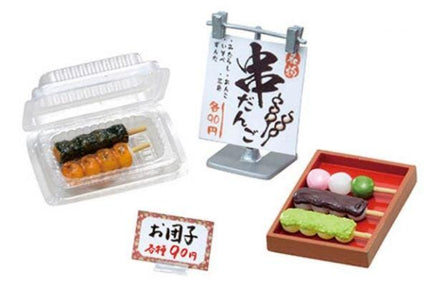 various food items, including a plastic container with sushi, a sign with Japanese text, and a wooden tray with different types of food.