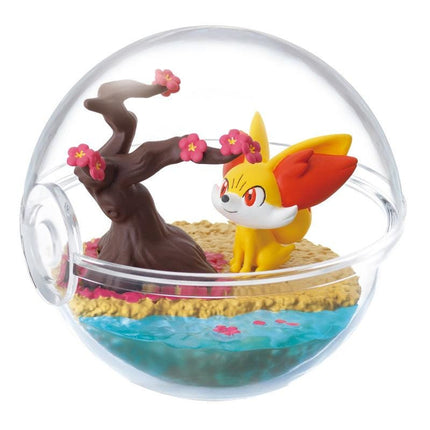 A figurine of a cat-like creature with yellow and red colors, sitting on a miniature landscape with a tree, flowers, and water.