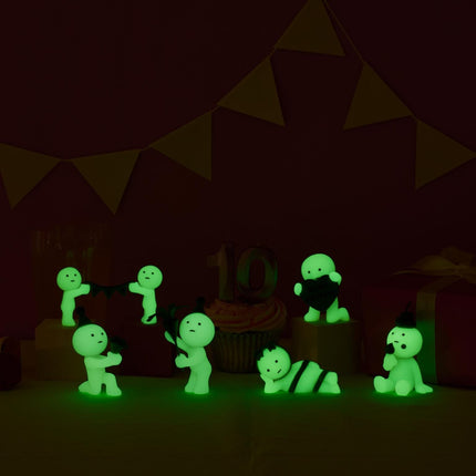 A collection of small, glowing figurines in various poses, including one holding a cupcake, set against a dark background with triangular flags.