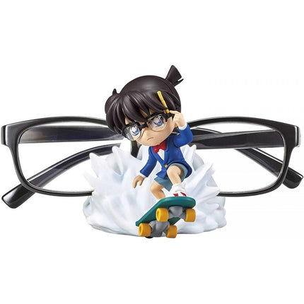 A figurine of a person wearing glasses and a blue jacket is depicted riding a skateboard, with a pair of glasses in the background.