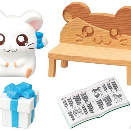 a white hamster figurine, a wooden bench, a gift box with a blue ribbon, and a book with illustrations of hamsters.