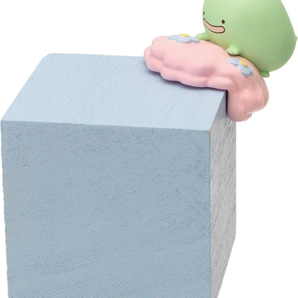 A small green toy figurine is perched on the edge of a light blue wooden block.