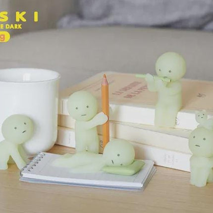 a collection of small, glowing figurines arranged on a wooden surface, along with a white mug and a stack of books.