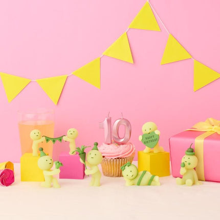 a pink background with yellow triangular flags, a cupcake with a number 10 candle, and various small figurines, including a baby figurine and a cupcake with a number 10 candle.