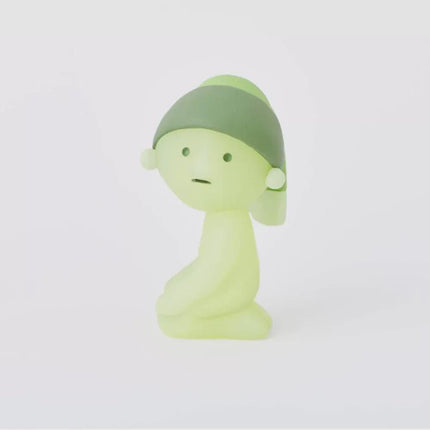 A small, green figurine with a pensive expression is sitting on its knees against a plain white background.