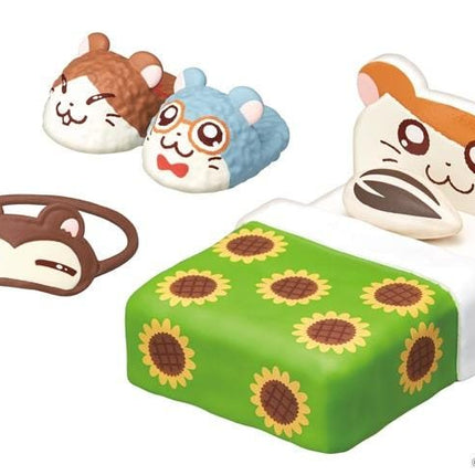 A collection of small toy figurines, including a hamster-shaped bed, a cat-shaped slipper, and a sunflower-patterned bedspread.