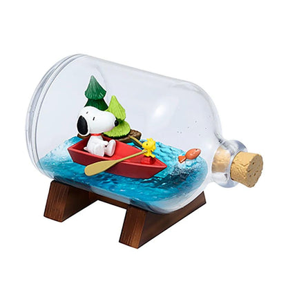 A glass bottle containing a miniature scene with a Snoopy dog character sitting in a red boat, surrounded by a small fish and a yellow bird.
