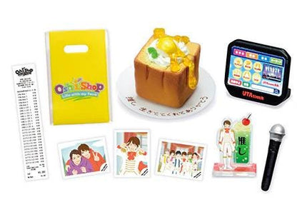 various objects, including a yellow bag, a cake with a yellow topping, a black electronic device, a microphone, and several small pictures or illustrations.