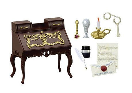 a brown desk with gold accents, a pair of glasses, a candle, a pen, and some papers.