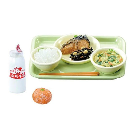 A tray containing a variety of Japanese dishes, including rice, meat, and vegetables, accompanied by a bottle of milk and a small orange.