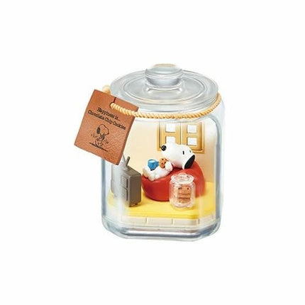 A glass jar containing a miniature scene with a Snoopy figurine sitting on a couch, a television, and a small jar of cookies.