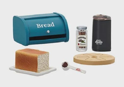 a blue bread box, a jar of spices, a black coffee mug, a loaf of bread, a spoon, and a wooden cutting board.