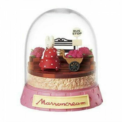 A pink and clear snow globe containing a miniature scene with a small white rabbit, a bus stop sign, and a wheelbarrow filled with flowers.