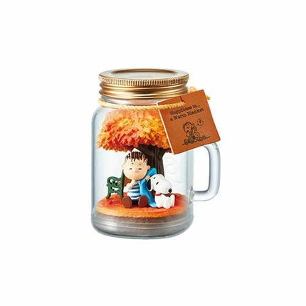 A glass jar containing a miniature scene with a young boy sitting on a bench under a tree, accompanied by a dog.