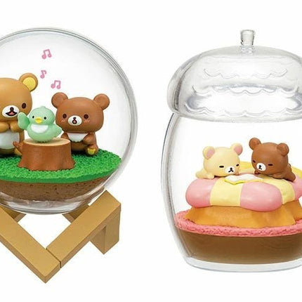 two glass figurines, each containing a small bear and a bird, set against a natural landscape.