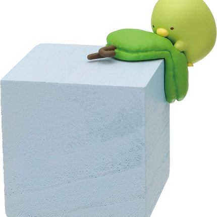 A small green toy figurine is perched on top of a gray block.