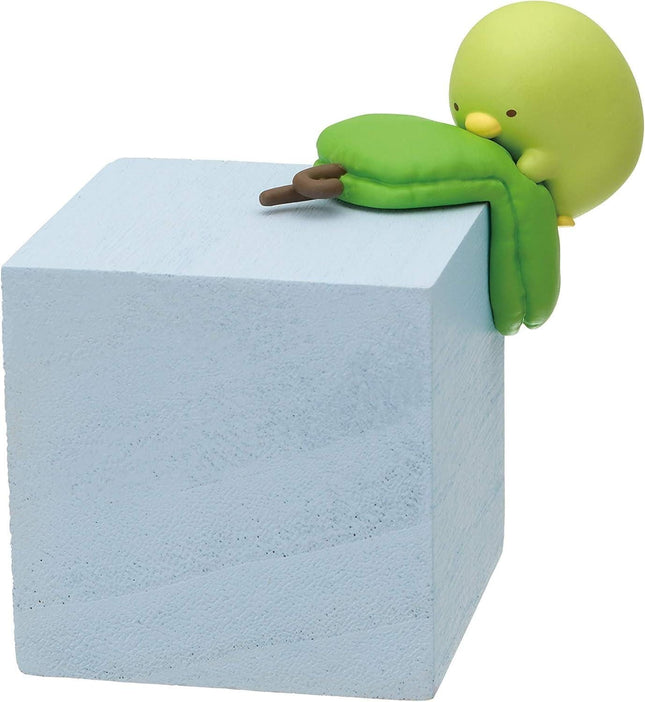 A small green toy figurine is perched on top of a gray block.