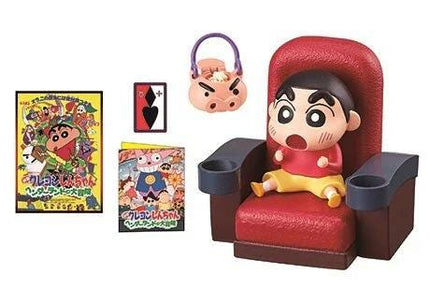 A toy figurine of a boy sitting in a red chair, with a toy bag and a toy card hanging nearby.